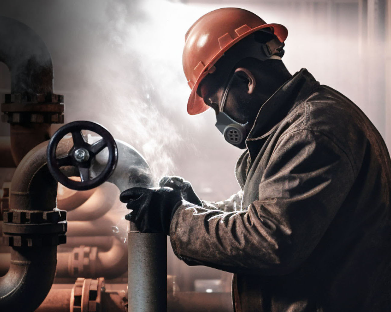 Worker in an orange hard hat, wearing a respirator mask and gloves, adjusting a valve on a pipe in an industrial setting with steam or mist in the background.